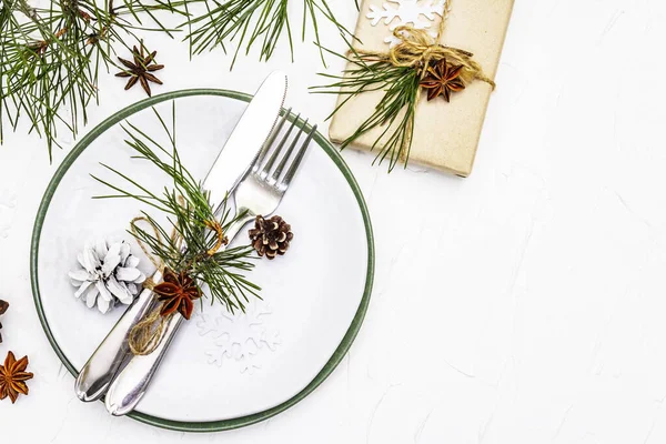 Noel ya da yeni yıl sofrası. Şenlikli çatal bıçak takımı, taze çam dallı seramik tabaklar, koniler, sıfır atık hediye ve yıldız anason. Beyaz macun arkaplan, üst görünüm