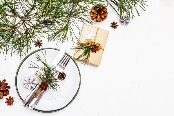 Noel ya da yeni yıl sofrası. Şenlikli çatal bıçak takımı, taze çam dallı seramik tabaklar, koniler, sıfır atık hediye ve yıldız anason. Beyaz macun arkaplan, üst görünüm