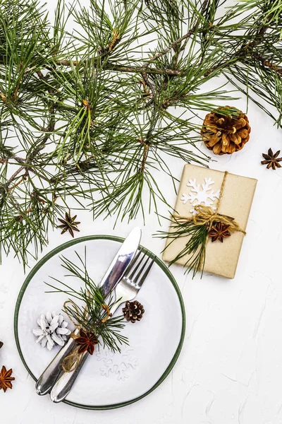 Noel ya da yeni yıl sofrası. Şenlikli çatal bıçak takımı, taze çam dallı seramik tabaklar, koniler, sıfır atık hediye ve yıldız anason. Beyaz macun arkaplanı, kapat