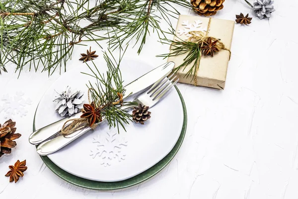 Noel ya da yeni yıl sofrası. Şenlikli çatal bıçak takımı, taze çam dallı seramik tabaklar, koniler, sıfır atık hediye ve yıldız anason. Beyaz macun arkaplanı, kopyalama alanı
