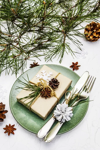 Noel ya da yeni yıl sofrası. Şenlikli çatal bıçak takımı, taze çam dallı seramik tabaklar, koniler, sıfır atık hediye ve yıldız anason. Beyaz macun arkaplanı, kapat