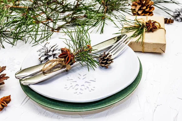 Noel ya da yeni yıl sofrası. Şenlikli çatal bıçak takımı, taze çam dallı seramik tabaklar, koniler, sıfır atık hediye ve yıldız anason. Beyaz macun arkaplanı, kapat