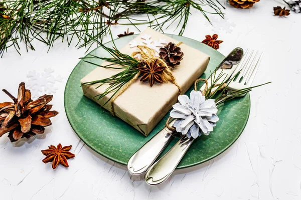 Noel ya da yeni yıl sofrası. Şenlikli çatal bıçak takımı, taze çam dallı seramik tabaklar, koniler, sıfır atık hediye ve yıldız anason. Beyaz macun arkaplanı, kapat