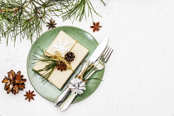 Noel ya da yeni yıl sofrası. Şenlikli çatal bıçak takımı, taze çam dallı seramik tabaklar, koniler, sıfır atık hediye ve yıldız anason. Beyaz macun arkaplan, üst görünüm