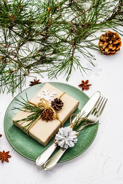 Noel ya da yeni yıl sofrası. Şenlikli çatal bıçak takımı, taze çam dallı seramik tabaklar, koniler, sıfır atık hediye ve yıldız anason. Beyaz macun arkaplanı, kapat