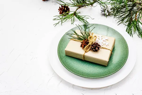 Noel ya da yeni yıl sofrası. Şenlikli çatal bıçak takımı, taze çam dallı seramik tabaklar, koniler, sıfır atık hediye ve yıldız anason. Beyaz macun arkaplanı, kopyalama alanı