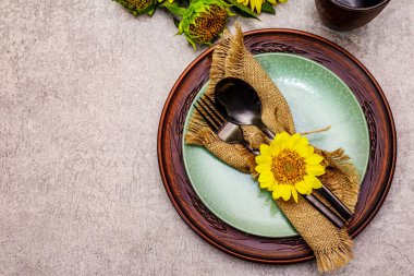 Sonbahar ve Şükran Günü yemeği. Ayçiçeği buketi, seramik tabaklar ve çuval bezi peçete. Taş zeminde siyah çatal bıçak takımı, üst görünüm.