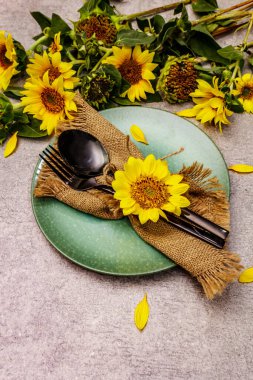 Sonbahar ve Şükran Günü yemeği. Ayçiçeği buketi, seramik tabak ve çuval bezi peçete. Taş zemine siyah çatal bıçak takımı, kopyala boşluk
