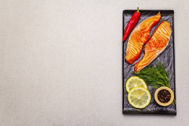 Çiğ Norveç alabalık filetosu. Bir parça taze balık, limon, dereotu, acı biber, tuz. Suşi derecesi, taş beton arka plan