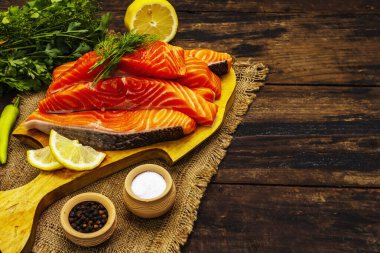 Çiğ Norveç alabalığı. Taze balık parçaları, limon, dereotu, biber, yeşillik, tuz. Eski tahta masa.