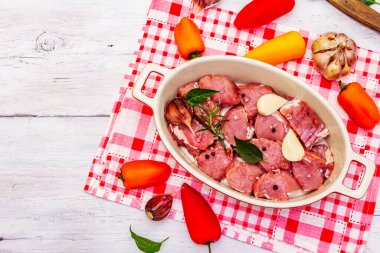 Çiğ dana eti, sebzeler ve pişirmeye hazır diğer malzemelerle birlikte parçalara ayrıldı. Beyaz ahşap kırsal masa, organik mutfak konsepti, üst manzara.