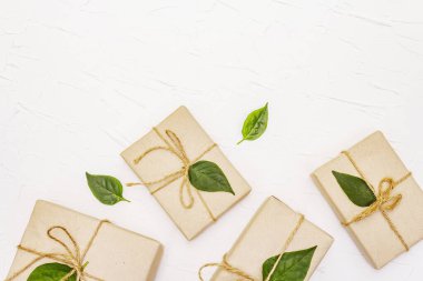 Sıfır atık hediye konsepti. Beyaz macun arka planında el işi kutularının ve yeşil yaprakların yaratıcı düzenleme çerçevesi, üst görünüm