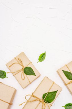Sıfır atık hediye konsepti. Beyaz macun arka planında el işi kutularının ve yeşil yaprakların yaratıcı düzenleme çerçevesi, üst görünüm
