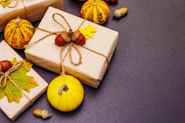 Sıfır atık hediye konsepti. Karton kutular, mini balkabakları, meşe palamutları ve dökülen yapraklarla yaratıcı bir sonbahar dekoru. Şükran Günü ya da Cadılar Bayramı kavramı siyah taş arka plan, üst görünüm