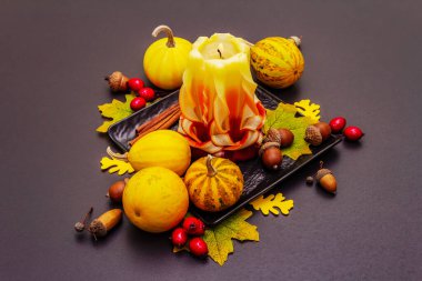 Şükran Günü veya Cadılar Bayramı için sonbahar kompozisyonu. Yanan mumlar, olgun balkabakları, meşe palamutları, dökülen yapraklar ve gül üzümü. Taş beton arkaplan, kopyalama alanı