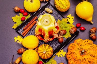 Şükran Günü veya Cadılar Bayramı için sonbahar kompozisyonu. Yanan mumlar, olgun balkabakları, meşe palamutları, dökülen yapraklar ve gül üzümü. Taş beton zemin, üst görünüm