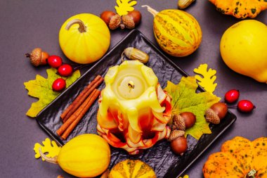 Şükran Günü veya Cadılar Bayramı için sonbahar kompozisyonu. Yanan mumlar, olgun balkabakları, meşe palamutları, dökülen yapraklar ve gül üzümü. Taş beton arka plan, kapat