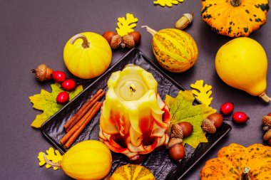 Şükran Günü veya Cadılar Bayramı için sonbahar kompozisyonu. Yanan mumlar, olgun balkabakları, meşe palamutları, dökülen yapraklar ve gül üzümü. Taş beton arka plan, kapat