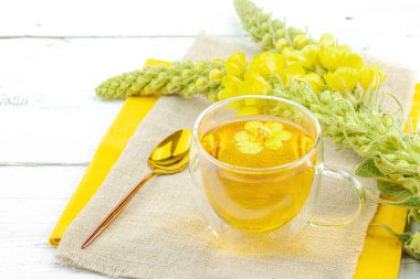 Doğal ahşap zemin üzerinde cam bir bardak Mullein bitkisel çayı ve keten kumaş üzerinde taze sarı Verbascum thapsus çiçekleri. Çevre sağlığı sahnesi, alternatif yaşam tarzı, kopyalama alanı