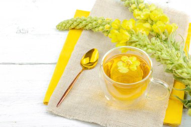 Doğal ahşap zemin üzerinde cam bir bardak Mullein bitkisel çayı ve keten kumaş üzerinde taze sarı Verbascum thapsus çiçekleri. Çevre sağlığı sahnesi, alternatif yaşam tarzı, kopyalama alanı