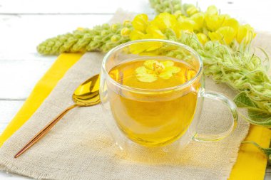 Doğal ahşap zemin üzerinde cam bir bardak Mullein bitkisel çayı ve keten kumaş üzerinde taze sarı Verbascum thapsus çiçekleri. Çevre sağlığı sahnesi, alternatif yaşam tarzı, yakın çekim.