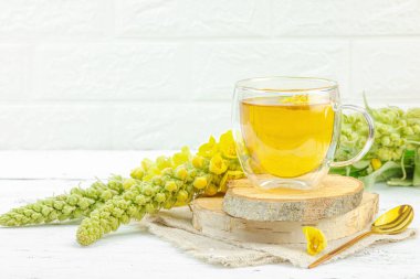 Doğal ahşap zemin üzerinde cam bir bardak Mullein bitkisel çayı ve keten kumaş üzerinde taze sarı Verbascum thapsus çiçekleri. Çevre sağlığı sahnesi, alternatif yaşam tarzı, kopyalama alanı