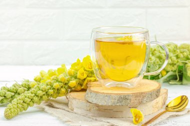 Doğal ahşap zemin üzerinde cam bir bardak Mullein bitkisel çayı ve keten kumaş üzerinde taze sarı Verbascum thapsus çiçekleri. Çevre sağlığı sahnesi, alternatif yaşam tarzı, kopyalama alanı