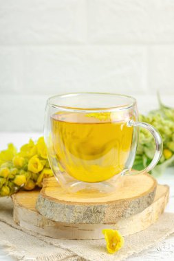 Doğal ahşap zemin üzerinde cam bir bardak Mullein bitkisel çayı ve keten kumaş üzerinde taze sarı Verbascum thapsus çiçekleri. Çevre sağlığı sahnesi, alternatif yaşam tarzı, kopyalama alanı