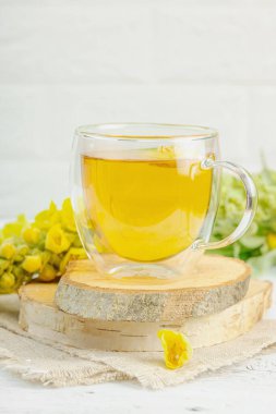 Doğal ahşap zemin üzerinde cam bir bardak Mullein bitkisel çayı ve keten kumaş üzerinde taze sarı Verbascum thapsus çiçekleri. Çevre sağlığı sahnesi, alternatif yaşam tarzı, kopyalama alanı