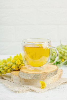 Doğal ahşap zemin üzerinde cam bir bardak Mullein bitkisel çayı ve keten kumaş üzerinde taze sarı Verbascum thapsus çiçekleri. Çevre sağlığı sahnesi, alternatif yaşam tarzı, kopyalama alanı