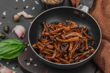 Tavada sarımsak, fesleğen ve baharatla kızartılmış Shimeji mantarı. Koyu bir arka planda, ahşap bir tahtayla servis ediliyor. Vejetaryen yaşam tarzı konsepti, düz yatak, yakın çekim