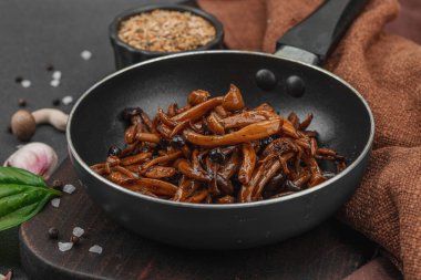 Tavada sarımsak, fesleğen ve baharatla kızartılmış Shimeji mantarı. Koyu bir arka planda, ahşap bir tahtayla servis ediliyor. Vejetaryen yaşam tarzı konsepti, düz yatak, yakın çekim