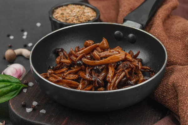 Tavada sarımsak, fesleğen ve baharatla kızartılmış Shimeji mantarı. Koyu bir arka planda, ahşap bir tahtayla servis ediliyor. Vejetaryen yaşam tarzı konsepti, düz yatak, yakın çekim