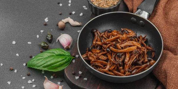 Tavada sarımsak, fesleğen ve baharatla kızartılmış Shimeji mantarı. Koyu bir arka planda, ahşap bir tahtayla servis ediliyor. Vegan yaşam tarzı konsepti, düz yatış, afiş biçimi