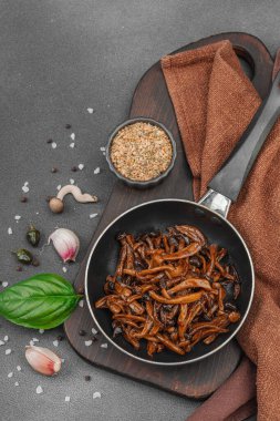 Tavada sarımsak, fesleğen ve baharatla kızartılmış Shimeji mantarı. Koyu bir arka planda, ahşap bir tahtayla servis ediliyor. Vejetaryen yaşam tarzı konsepti, düz yatak, üst manzara