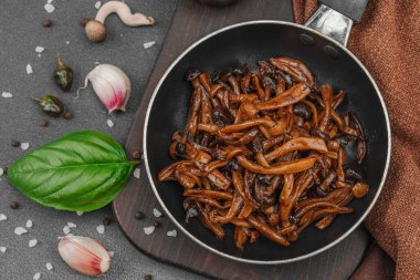 Tavada sarımsak, fesleğen ve baharatla kızartılmış Shimeji mantarı. Koyu bir arka planda, ahşap bir tahtayla servis ediliyor. Vejetaryen yaşam tarzı konsepti, düz yatak, üst manzara