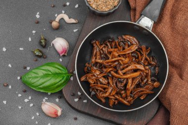 Tavada sarımsak, fesleğen ve baharatla kızartılmış Shimeji mantarı. Koyu bir arka planda, ahşap bir tahtayla servis ediliyor. Vejetaryen yaşam tarzı konsepti, düz yatak, üst manzara