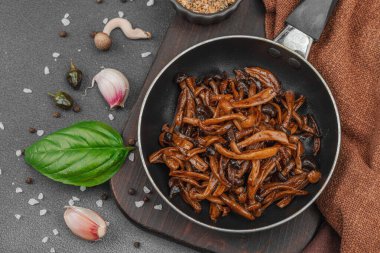 Tavada sarımsak, fesleğen ve baharatla kızartılmış Shimeji mantarı. Koyu bir arka planda, ahşap bir tahtayla servis ediliyor. Vejetaryen yaşam tarzı konsepti, düz yatak, üst manzara