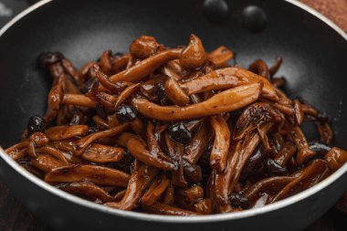 Tavada sarımsak, fesleğen ve baharatla kızartılmış Shimeji mantarı. Koyu bir arka planda, ahşap bir tahtayla servis ediliyor. Vejetaryen yaşam tarzı konsepti, düz yatak, yakın çekim