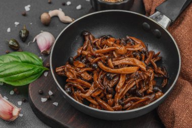 Tavada sarımsak, fesleğen ve baharatla kızartılmış Shimeji mantarı. Koyu bir arka planda, ahşap bir tahtayla servis ediliyor. Vejetaryen yaşam tarzı konsepti, düz yatak, yakın çekim