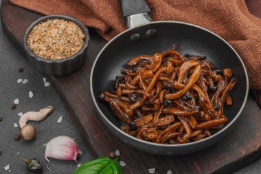 Tavada sarımsak, fesleğen ve baharatla kızartılmış Shimeji mantarı. Koyu bir arka planda, ahşap bir tahtayla servis ediliyor. Vejetaryen yaşam tarzı konsepti, düz yatak, yakın çekim