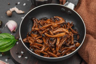 Tavada sarımsak, fesleğen ve baharatla kızartılmış Shimeji mantarı. Koyu bir arka planda, ahşap bir tahtayla servis ediliyor. Vejetaryen yaşam tarzı konsepti, düz yatak, yakın çekim