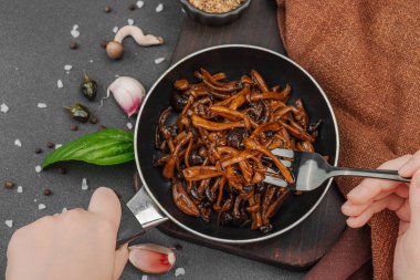 Tavada sarımsak, fesleğen ve baharatla kızartılmış Shimeji mantarı. Koyu bir arka planda, ahşap bir tahtayla servis ediliyor. El çatal, vejetaryen yaşam tarzı konsepti, üst görünüm.