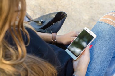 Tırnakları boyalı, elinde akıllı telefon tutan ve ekranı kapalı genç bir kız.