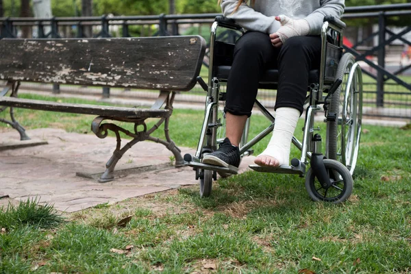 Person injured in a wheelchair. Foot and hand bandages, outdoor photography in a park