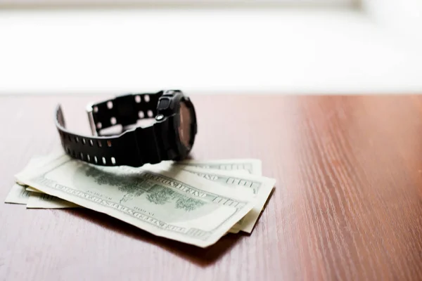 Время деньги. Сто долларов и черные часы на деревянном столе . — стоковое фото