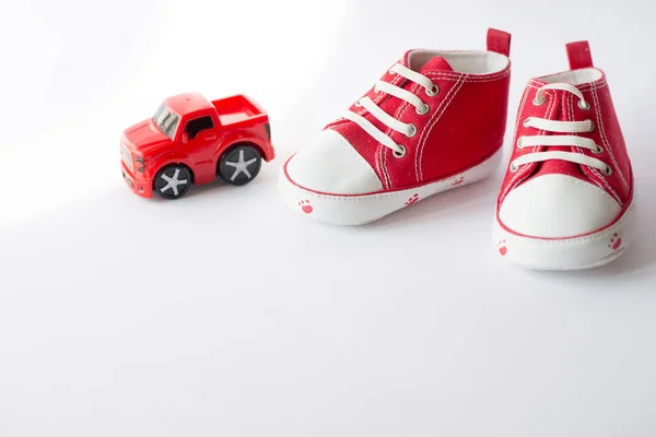 Cute red small sized canvas shoes with toy car top view on white background with copyspace