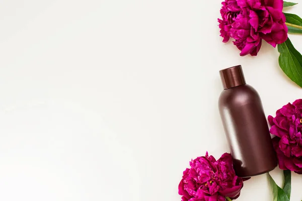 Cosmetic bottle with peony flowers on a white background with copy space.