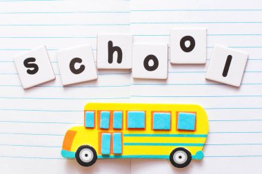Kelime Okulu siyah harflerle yazılmış beyaz kağıtlara ve parlak sarı oyuncak okul otobüsüne defter arkaplanına.