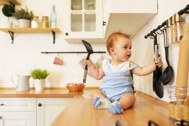 Bebek mutfak masasında tava ve kaşıkla oynuyor. Bir yaşında küçük bir çocuk metal aletlere çarpıyor.